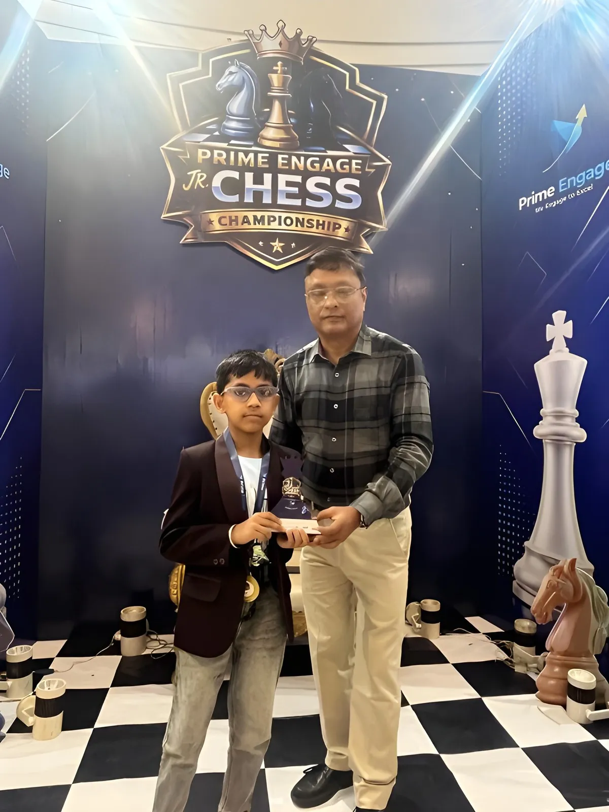 GM Dibyendu Barua presenting a trophy to a young player in front of the Prime Engage Jr. Chess Championship backdrop, Kolkata